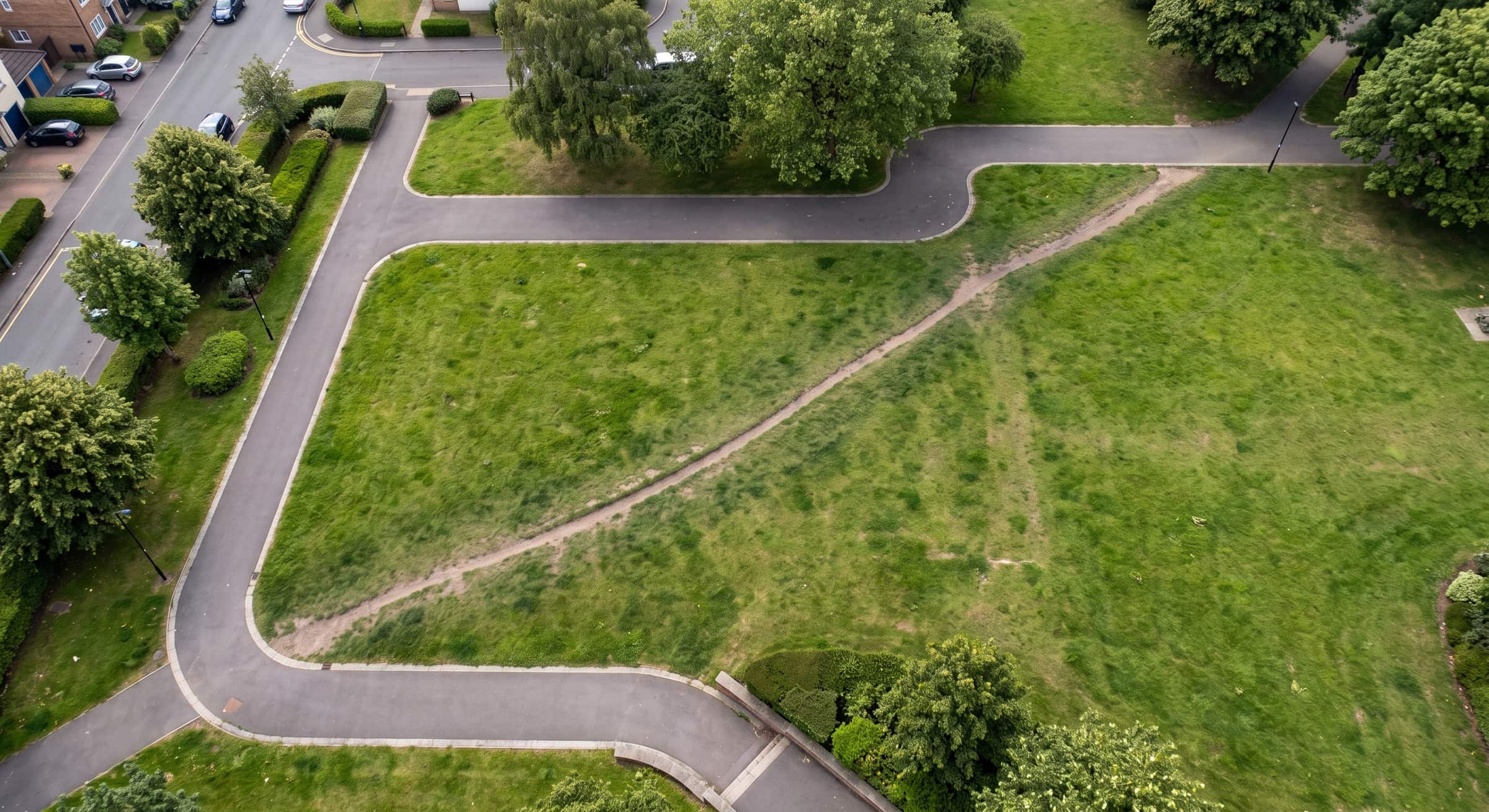 Luftbild: Ein asphaltierter Weg führt in einem Umweg um eine Rasenfläche herum, ein ausgetretener Pfad kürzt sie diagonal ab